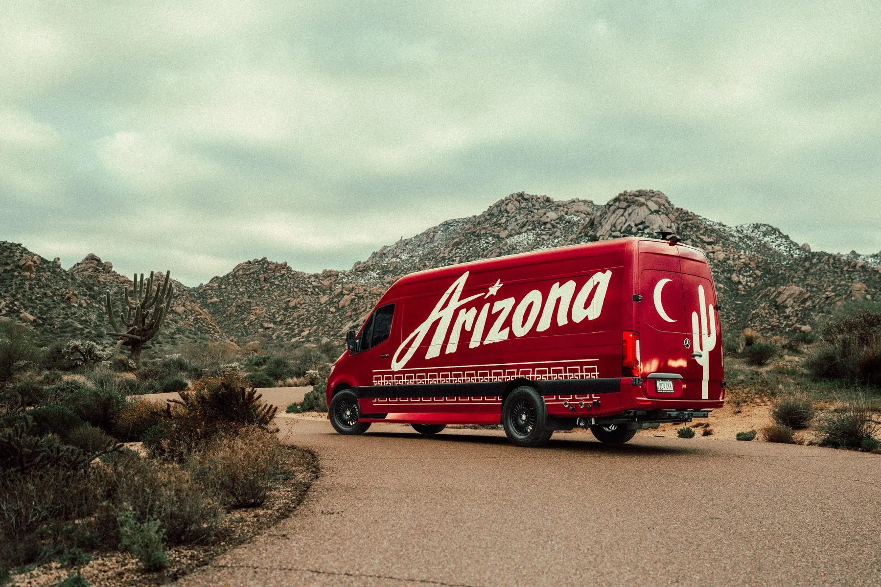 Custom wrapped van, rear three quarter in the daylight desert, saguaro and crescent moon graphics across the panel
