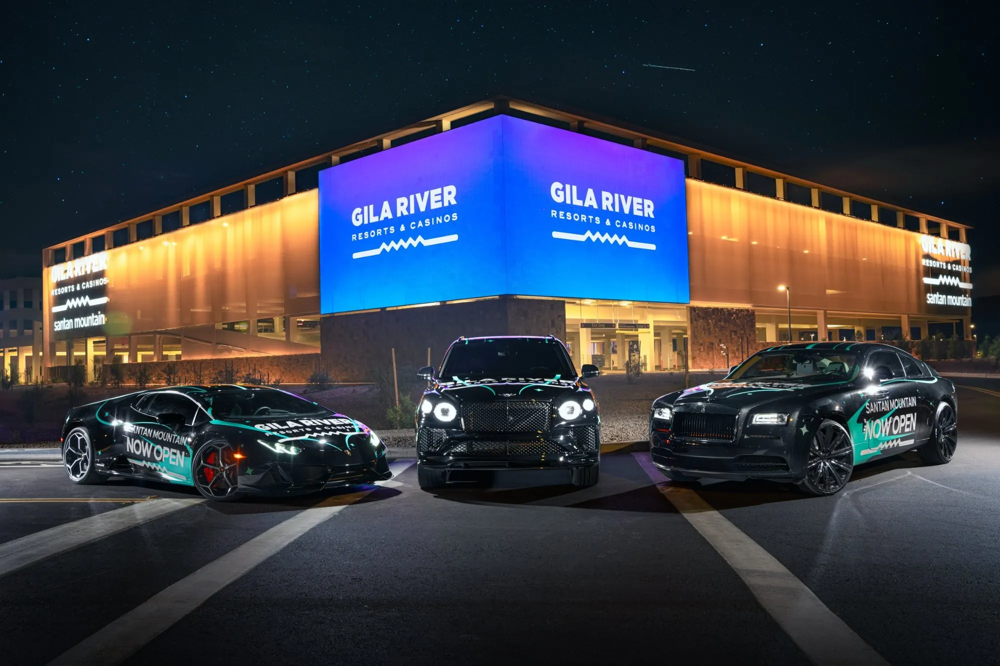Three wrapped supercars lined up outside a lit building at night, the facade screens burning behind them