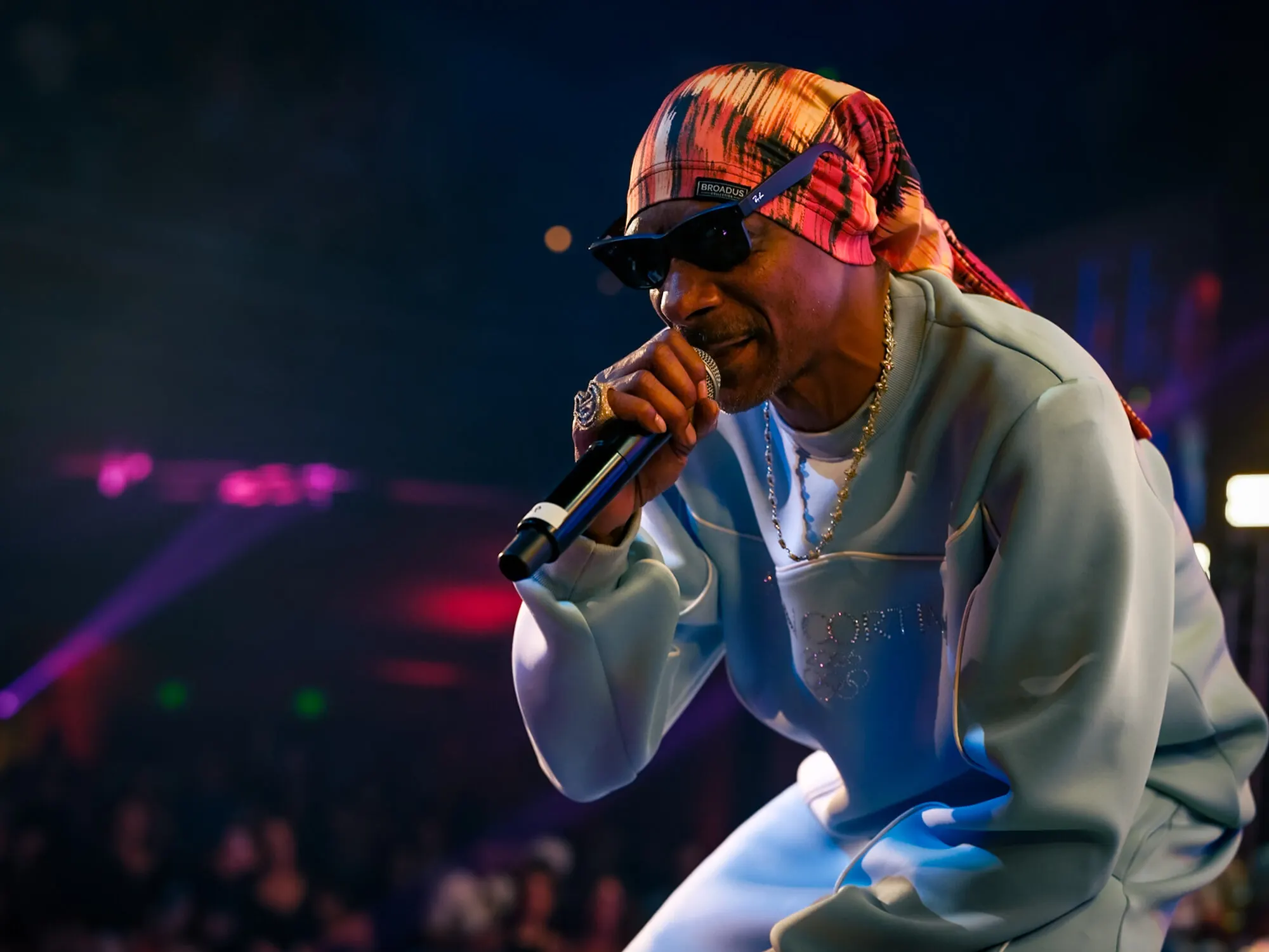 A performer at the microphone in a bandana and sunglasses, the crowd lit pink behind him