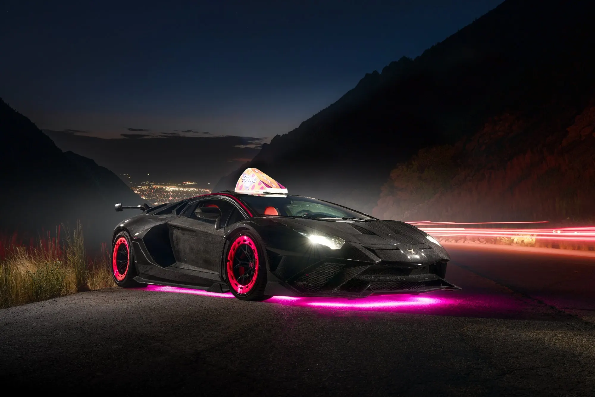 Black supercar with pink underglow on a canyon road at dusk, light trails running past it