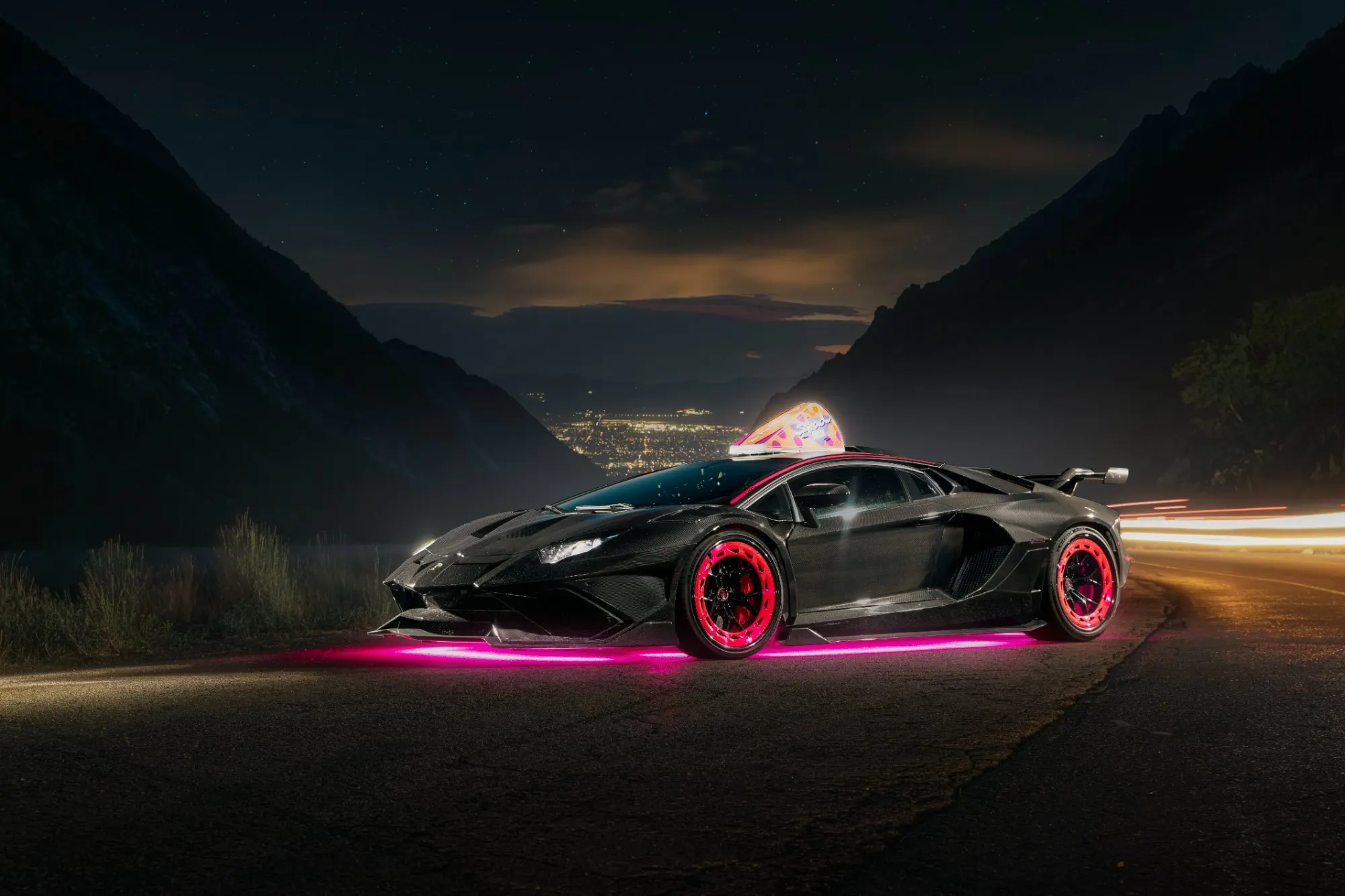 The same car from behind on the canyon road, valley lights far below