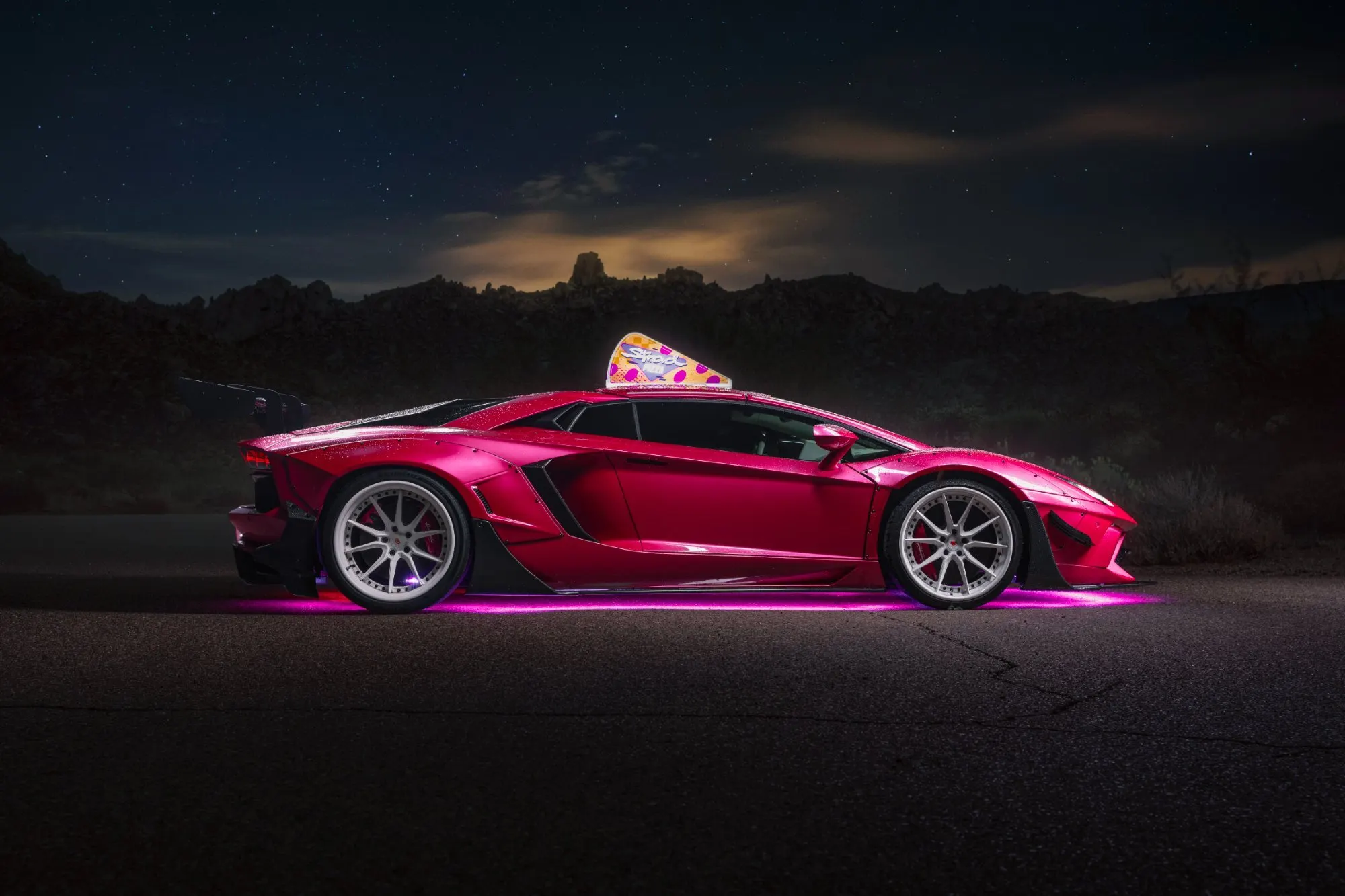 Magenta supercar in profile at night, its underglow washing the asphalt