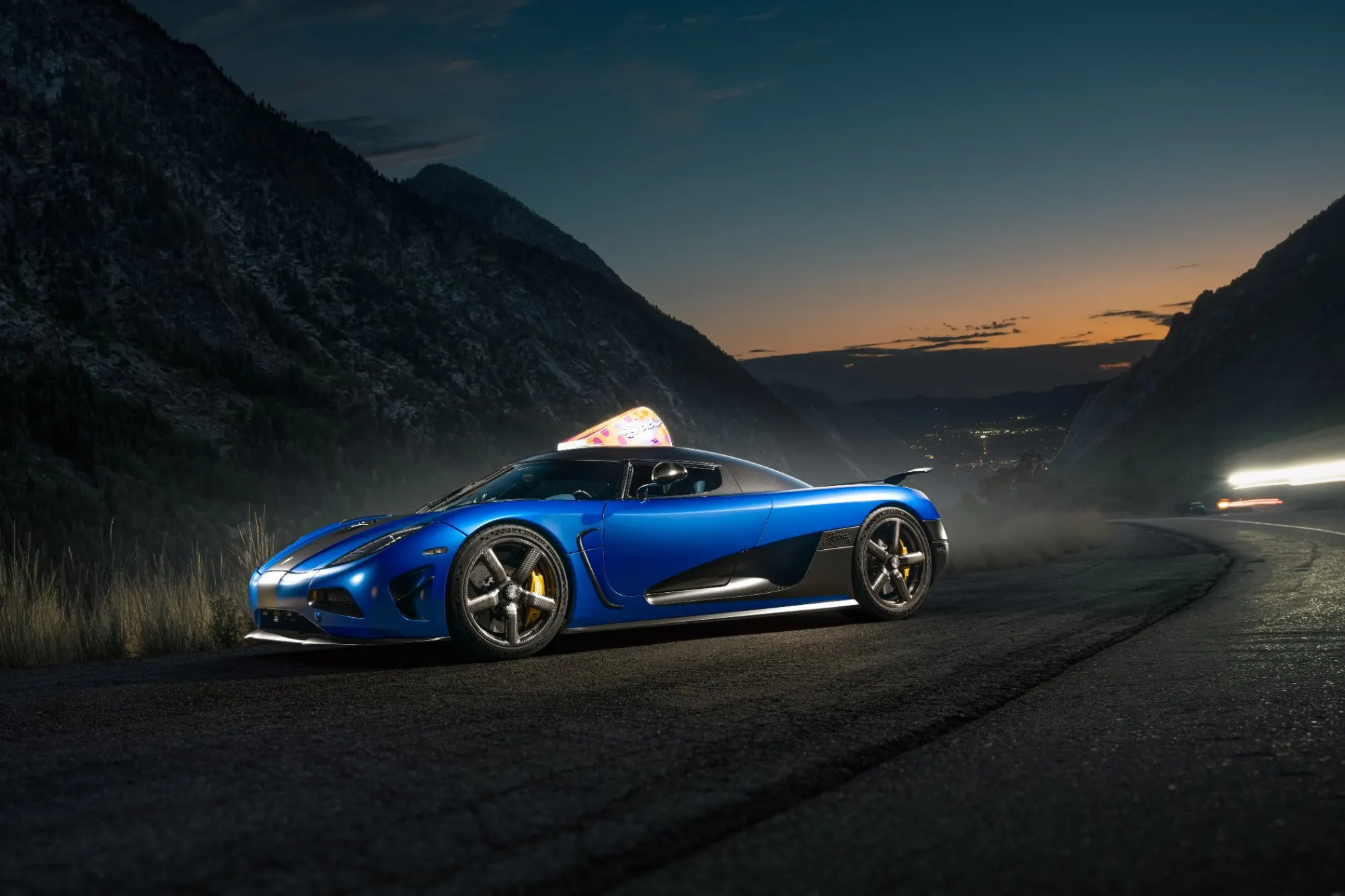 Blue hypercar in profile on a mountain road at sunset