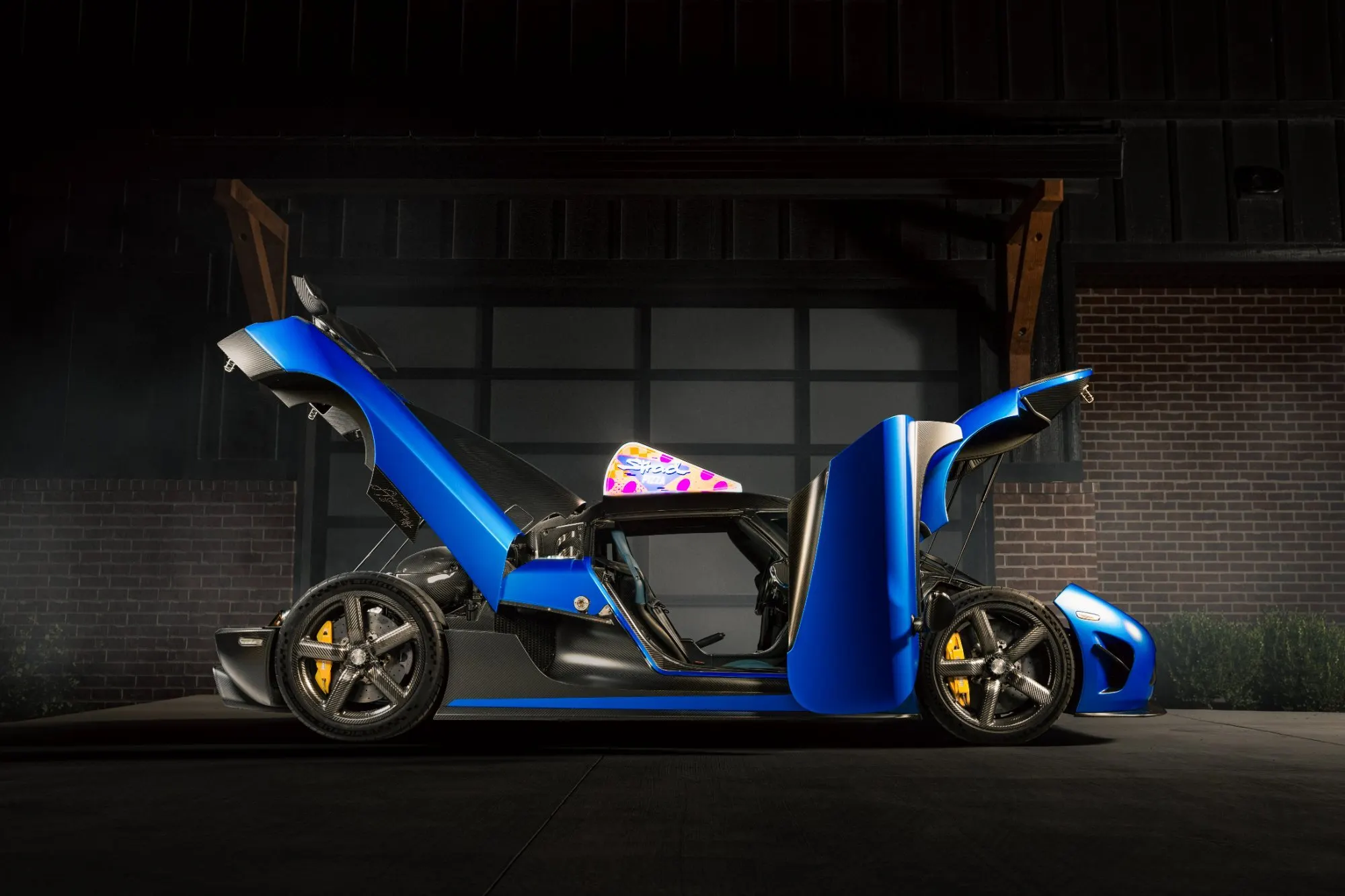 Blue hypercar in a dark garage, both doors and the rear clam open