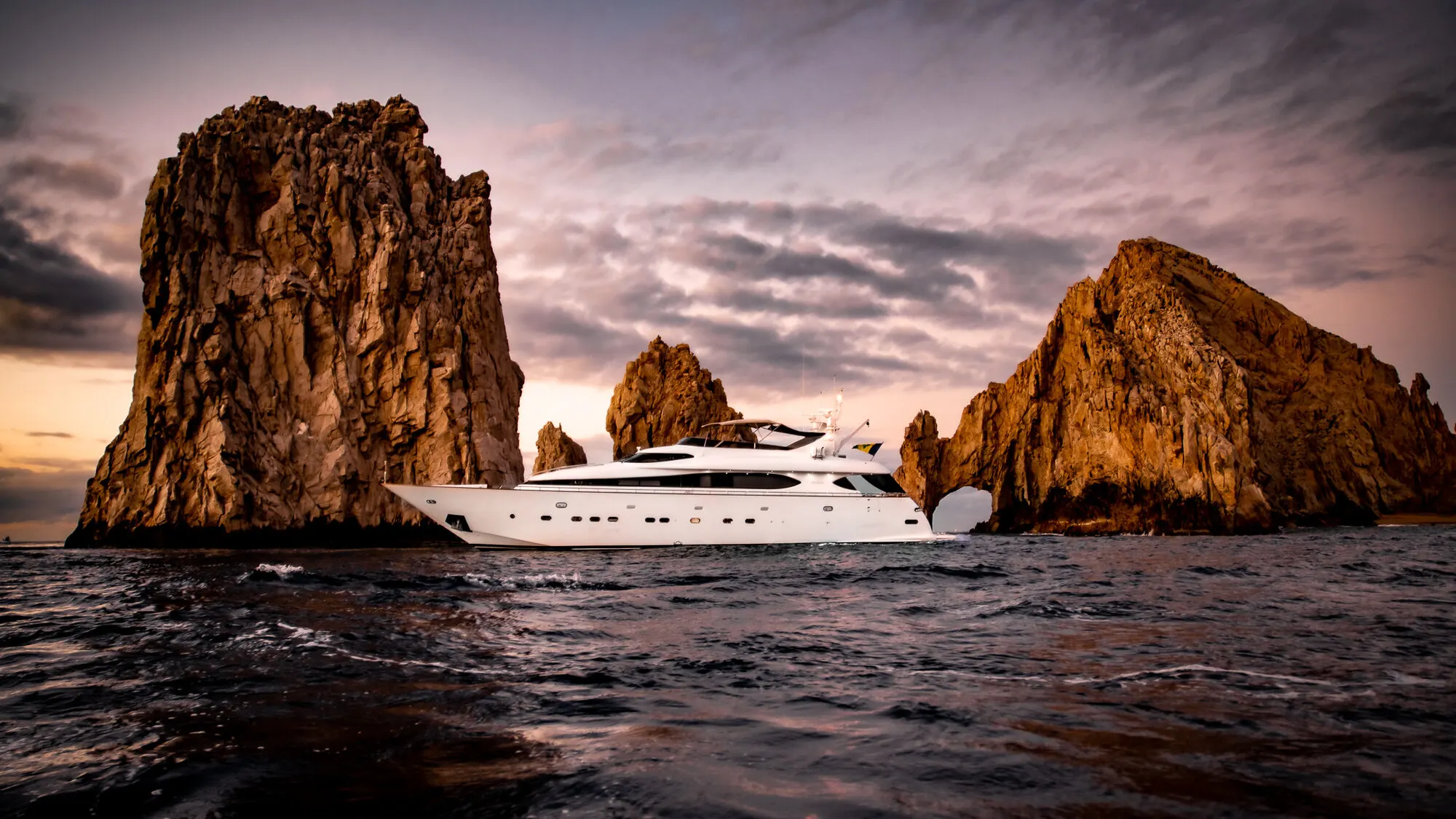 A yacht in profile off Cabo San Lucas, the Land’s End rock arch behind it in low sun